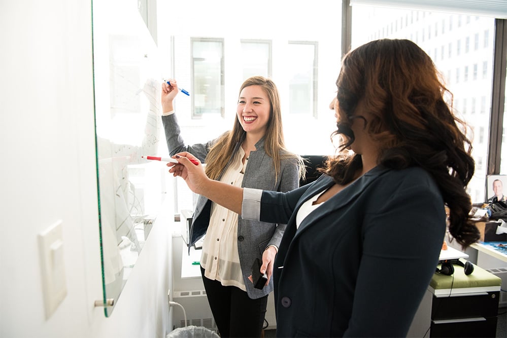 two female employees talking at a whiteboard