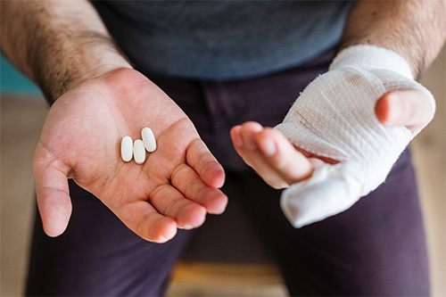 man with bandaged hand holding white pills